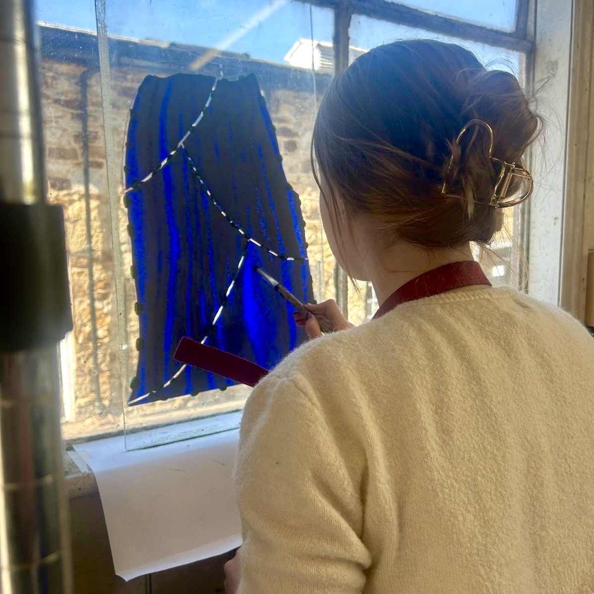 Photo showing the artist painting glass against a window.