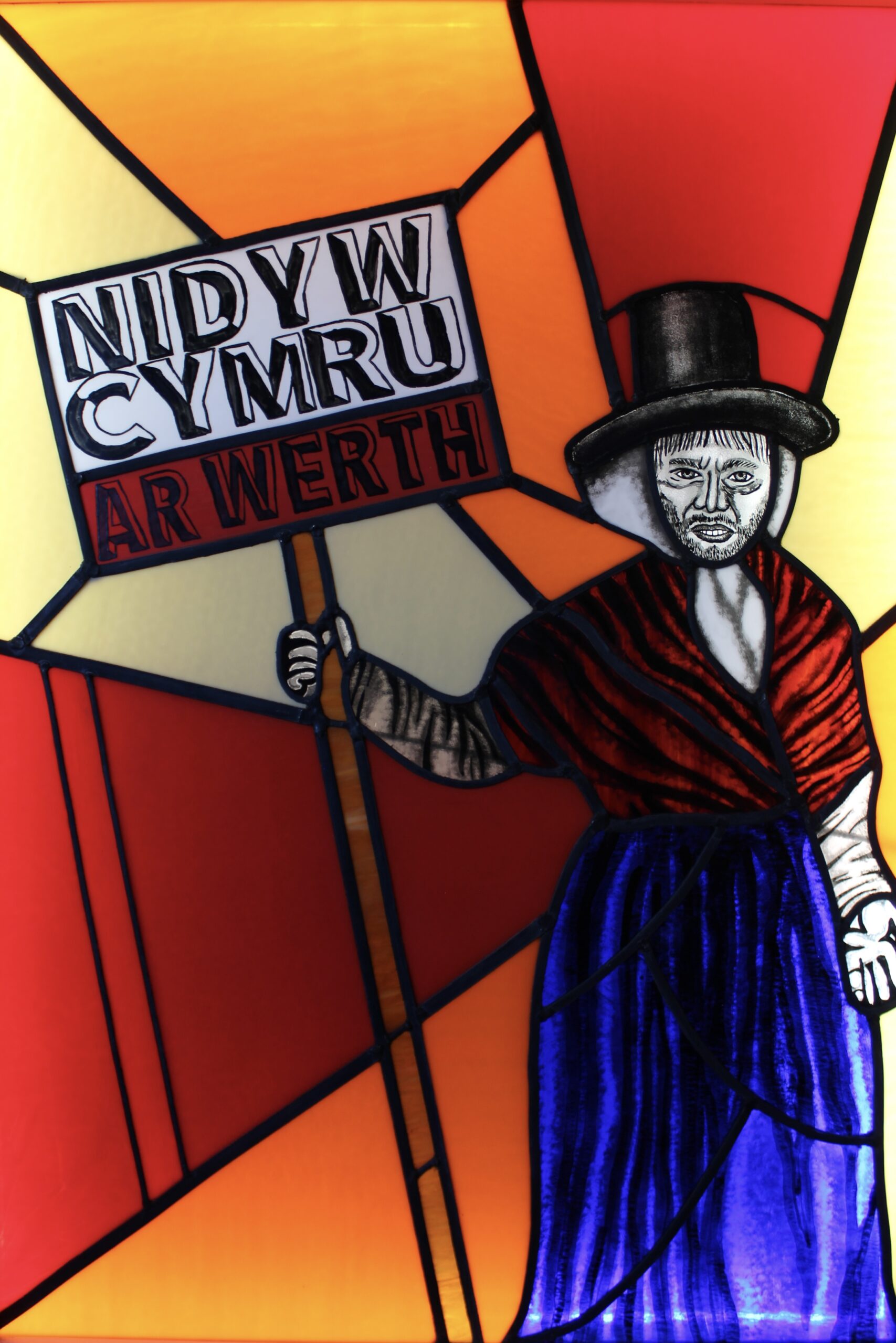 Photo of stained glass panel depicting man dressed up as a Welsh lady holding a protest sign.