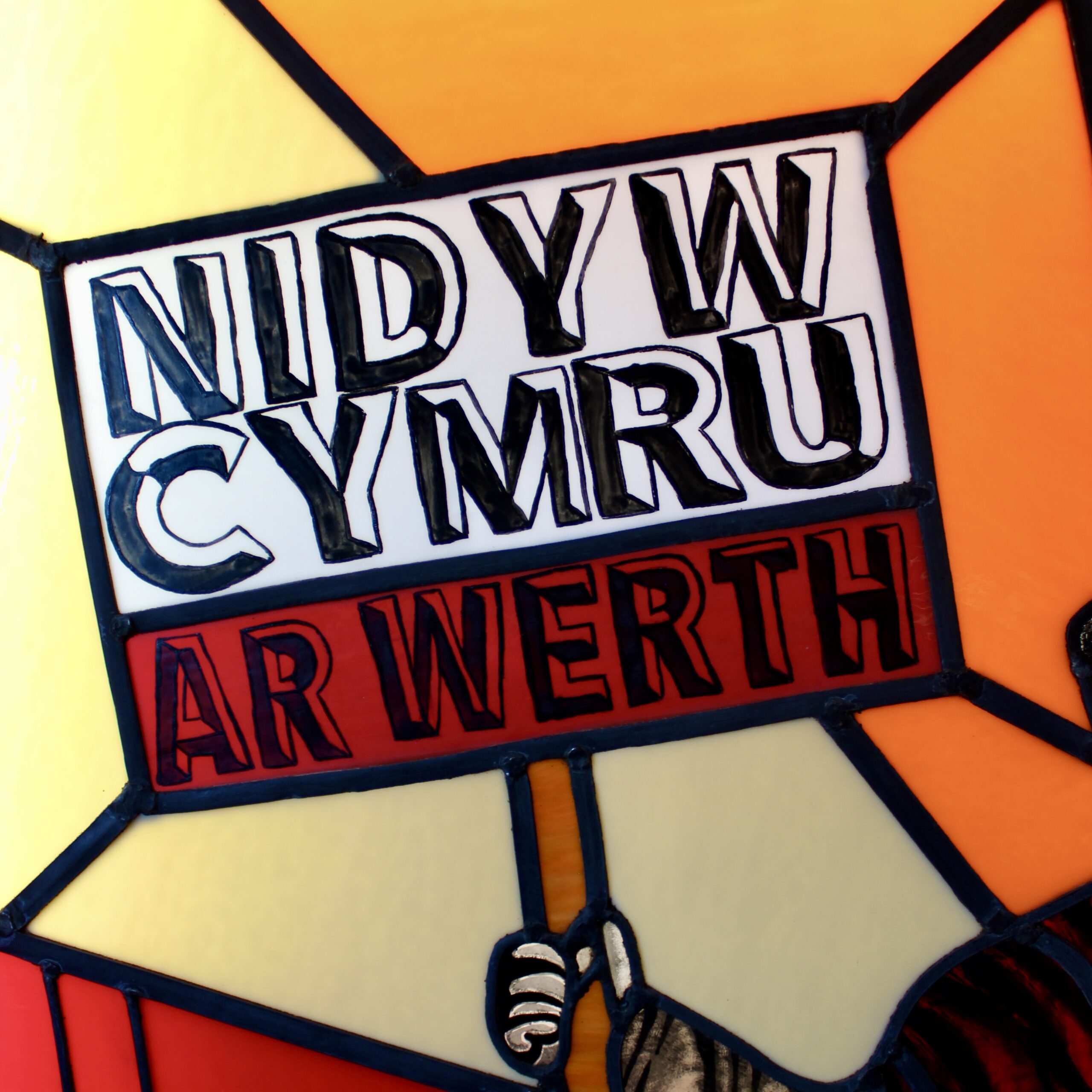 Photograph showing part of a stained glass panel, with a sign reading 'Nid Yw Cymru Ar Werth'.