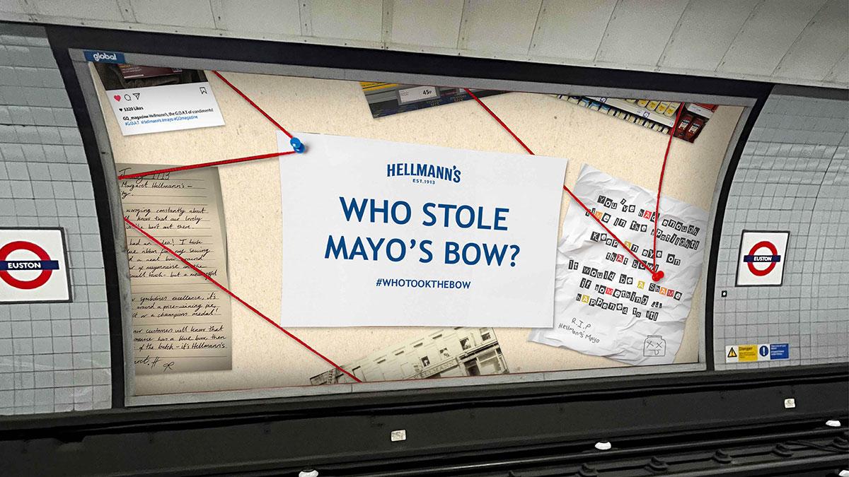 A Hellmann’s advertisement in a London Underground station with a mystery board design, asking “Who stole Mayo’s bow?” with red string linking clues, including handwritten notes and cut-out ransom text, promoting the hashtag #WhoTookTheBow.